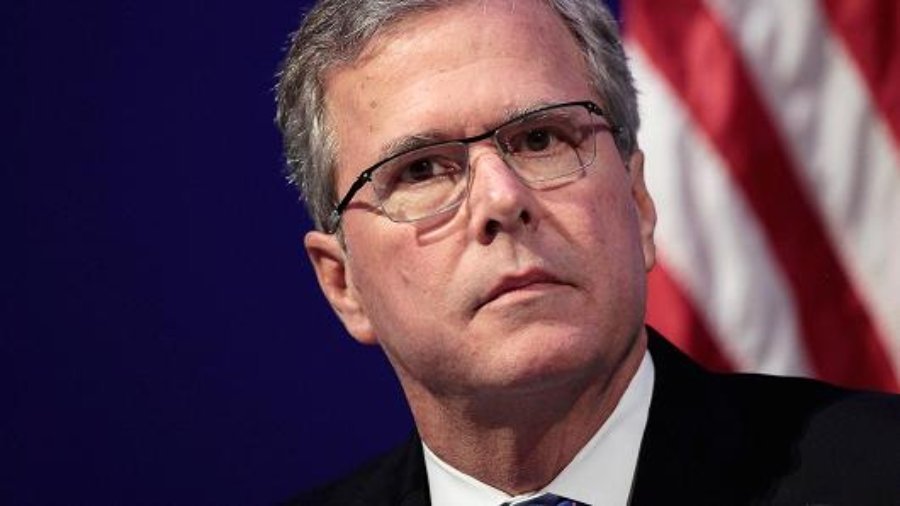 Jeb Bus looking at the camera wearing a suit in front of the American flag