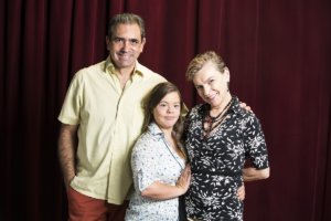 Cristina and her parents facing the camera and smiling with a red curtain behind them