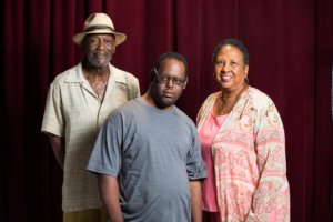 John Tucker and his parents facing the camera and smiling with a red curtain behind them