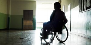 Individual in silhouette in a wheelchair in an empty hallway
