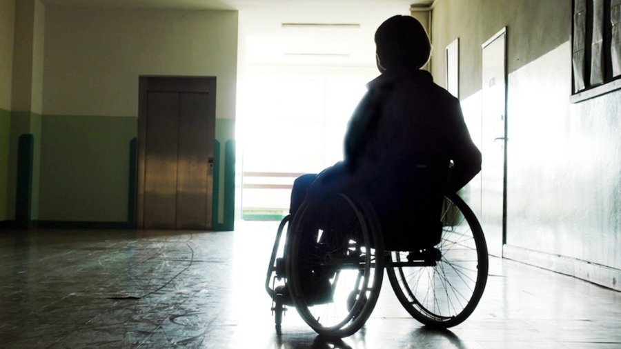 Individual in silhouette in a wheelchair in an empty hallway