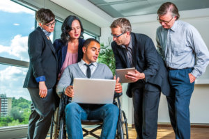 Five people - one in a wheelchair - looking at a computer in a business setting