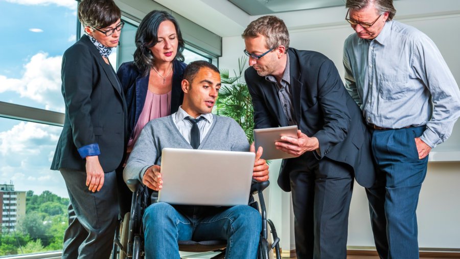 Five people - one in a wheelchair - looking at a computer in a business setting