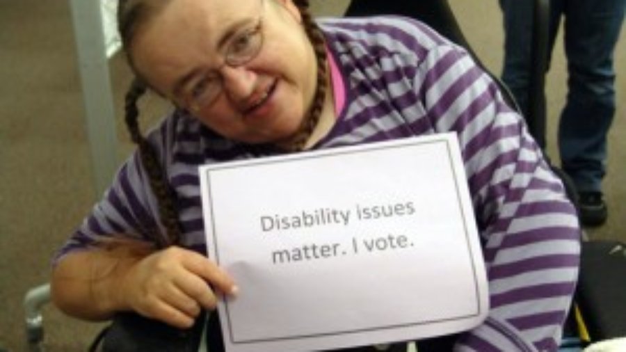 RespectAbility is asking all presidential candidates on both sides of the aisle to fill out a questionnaire and scorecard on disability issues. Image: Woman in wheelchair holding a sign that says: "Disability issues matter. I vote."