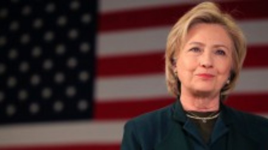 Hillary Clinton smiling with American flag as backdrop