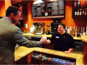 a woman with a disability working as a barista offers a customer a coffee as an example of the #RespectTheAbility campaign