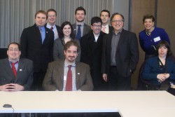 Fellows on a tour at NPR, posing together behind a table, half of the group seated and the other half standing behind