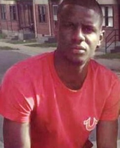 Headshot of Freddie Gray in a red t-shirt outside in front of homes
