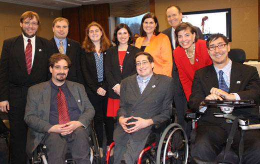 RespectAbility staff, fellows and board member smiling in a posed photograph. Three men and four women standing behind three men in wheelchairs. All are dressed formally in suits. 