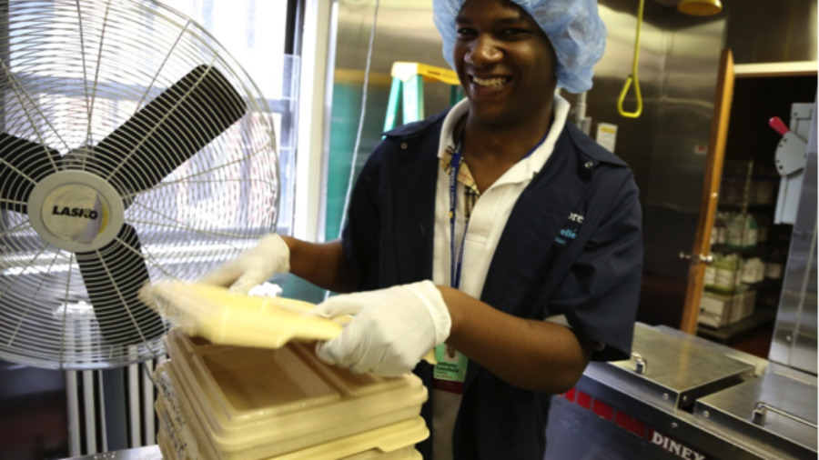 Image of man with hair net stacking trays in an industrial kitchen as example of #RespectTheAbility campaign