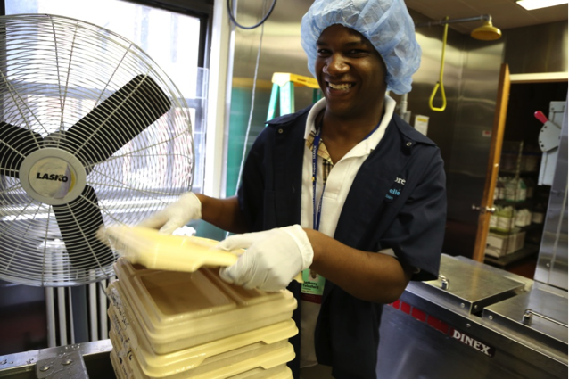 Image of man with hair net stacking trays in an industrial kitchen