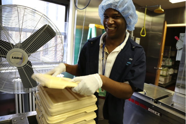 Image of man with hair net stacking trays in an industrial kitchen as example of #RespectTheAbility campaign