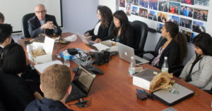 Curt Decker seated at head of brown table with Fellows seated around the other sides listening to him