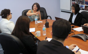 Donna seated at head of brown table with Fellows seated around the other sides listening to her