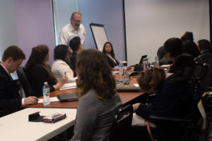 Jonathan Kessler standing next to a table full of college-age and young adults with and without disabilities seated around a table