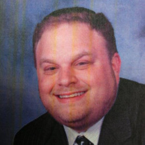 headshot of Aaron Orlofsky smiling and squiting eyes, wearing suit and tie color photo