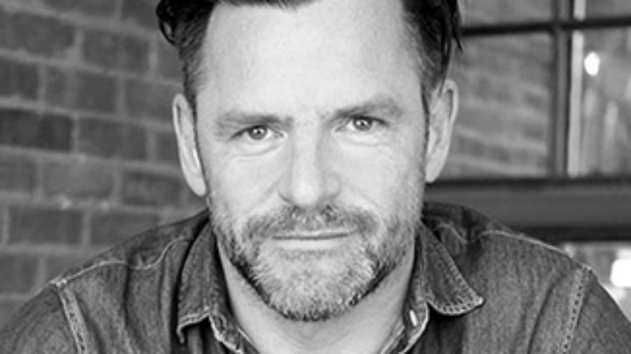 headshot of Andrew Egan leaning on a table wearing a button down shirt and facing the camera grayscale photo