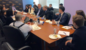 Andy Imparato seated at head of brown table with Fellows seated around the other sides listening to him