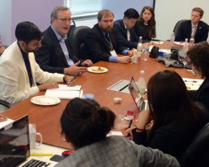 Andy Imparato seated at head of brown table with Fellows seated around the other sides listening to him