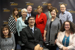 Smiling members of the Board of Directors and Advisors seated and standing in front of a RespectAbility banner