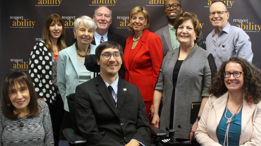 Smiling members of the Board of Directors and Advisors seated and standing in front of a RespectAbility banner
