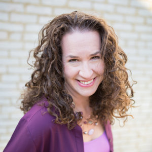 headshot of Dana Marlowe smiling at the camera she has long curly hair and she is wearing a purple sweater color photo