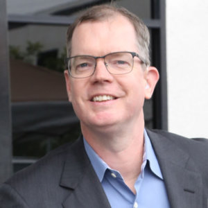 Delbert Whetter smiling wearing a suit jacket and glasses