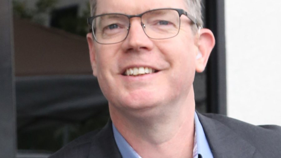 Delbert Whetter smiling wearing a suit jacket and glasses