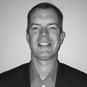 headshot of Delbert Whetter smiling and facing the camera wearing a button down shirt grayscale photo