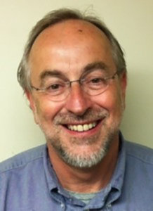 headshot of Doc Sweitzer smiling wearing glasses and a blue collared shirt, with a light beard and mustache color photo