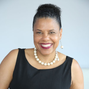 headshot of Donna Walton her hair is tied back and she is wearing a pearl necklace and pearl earrings, and smiling at the camera, color photo