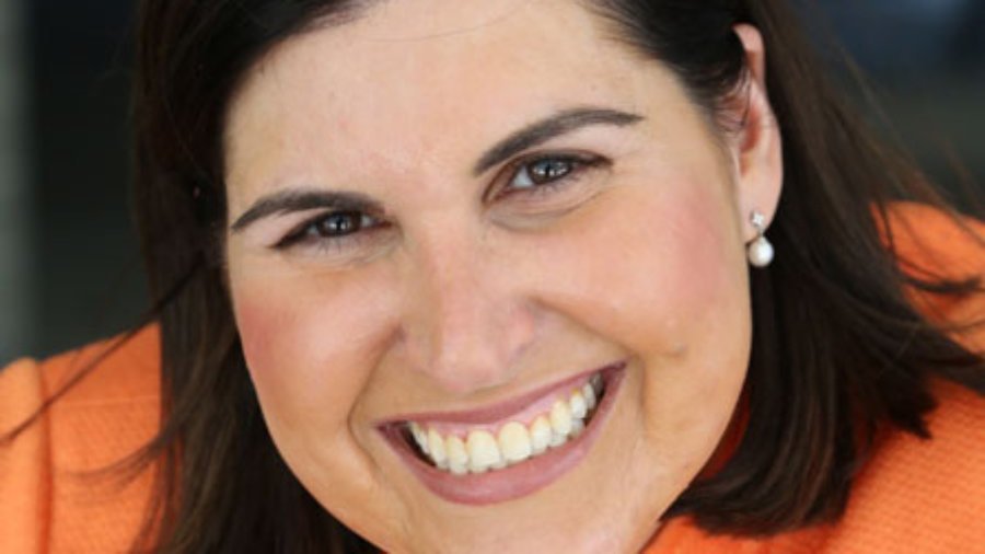 head shot of Lauren wearing an orange blazer, smiling and facing the camera color photo