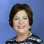 headshot of Linda Burger, who is smiling and wearing dangly earrings and a chunky necklace and a stripy shirt color photo