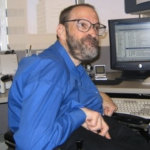 Neil Jacobson sitting at his computer and smiling he has a beard and is wearing glasses color photo