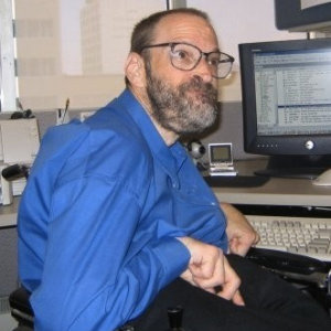 Neil Jacobson sitting at his computer and smiling he has a beard and is wearing glasses color photo