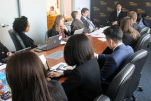 Randy Duchesneau seated at head of brown table with Fellows seated around the other sides listening to him