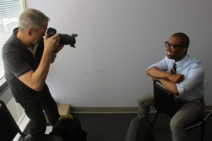 Rick Guidotti aiming his camera and taking a photo of Cal Harris who sits and poses for the picture