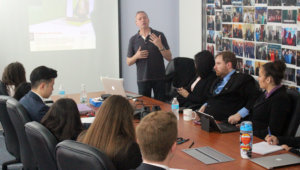 Rick Guidotti stands at the front of the room while fellows sit and listen to him speak