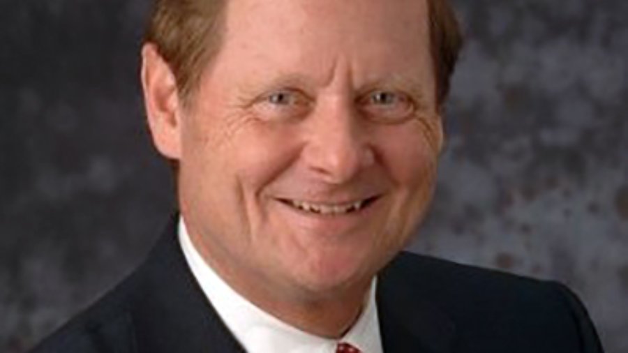 Steve Bartlett, has brown hair and he is smiling and wearing a black suit, white shirt, and red spotted tie and an american flag pin on his jacket, color photo