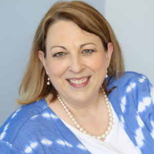 headshot of Tonya smiling with her hair loose, wearing pearl earrings and pearl necklace wearing a white top and a light blue cardigan color photo