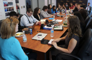 Mona Murray is at the head of the conference table speaking to all of the fellows who are looking in her direction.