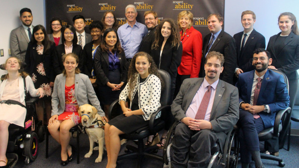 Richard Wolf pictured with RespectAbility Fellows and staff seated and standing in front of a RespectAbility banner