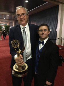 Bruce and Sean wearing tuxes, posing for the camera. Bruce holding an Emmy.