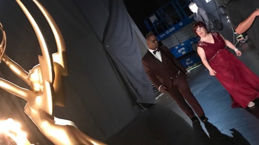 An African American man and a white woman dressed in a tux and gown back stage