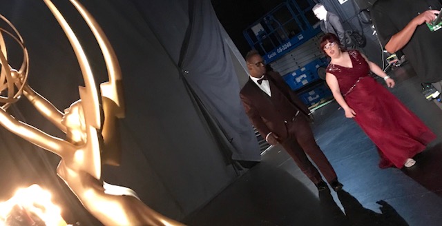 An African American man and a white woman dressed in a tux and gown back stage