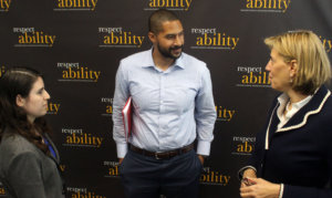 Three adults standing talking to one another in front of a banner saying RespectAbility