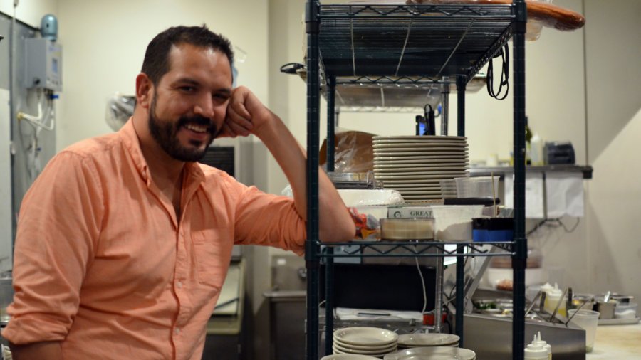 Dan Tapia wearing an orange shirt smiling and posing for the camera in the Fourth and Olive kitchen