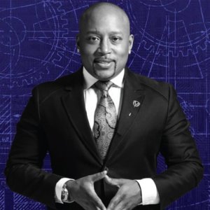 Daymond John in a black and white photo of him wearing a suit against a blue background