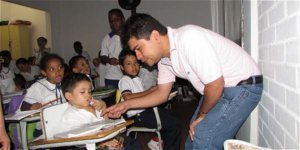 Jeison Aristizábal leaning ovr to help students seated at school desks