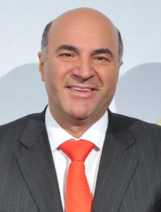 Kevin O'Leary headshot wearing a dark gray suit and a red tie